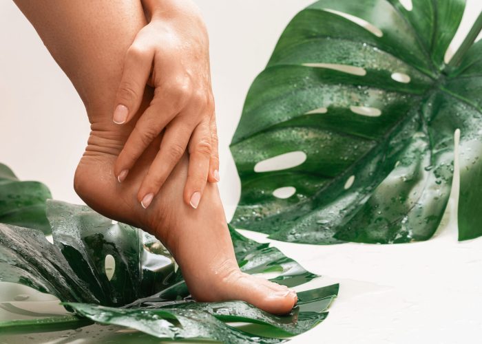 Closeup of wet female feet with smooth skin and Monstera deliciosa tropical leaf